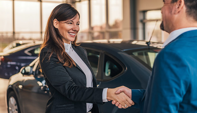 Cheerful car dealer handshake with customer in showroom.