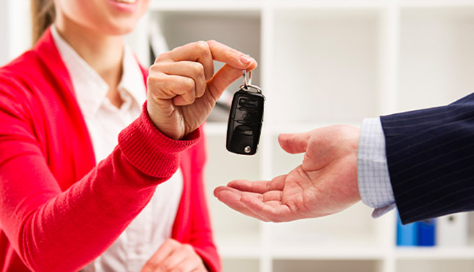 Female car agent giving key to male customer for test drive.
