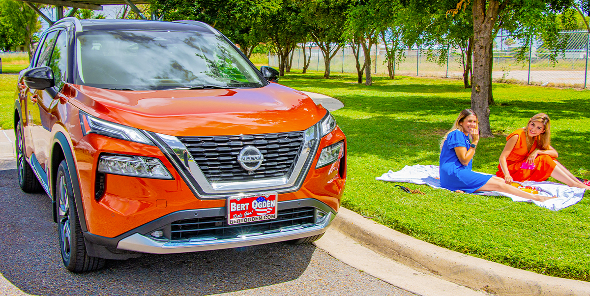 Two grils sitting on a blanket beside a Used Nissan Rogue
