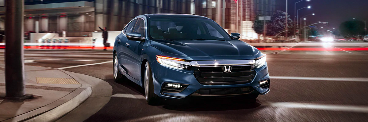 Front passenger-side view of 2021 Honda Insight Touring, in Cosmic Blue Metallic, driving on city road at night.