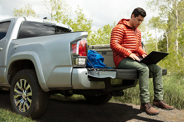 Man looking at his laptop while sitting on the back of a 2020 Toyota Tacoma